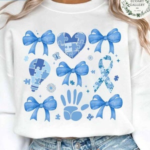 Peut inclure: Sweat-shirt blanc avec un motif de pièces de puzzle bleues. Le motif comprend un cœur, une ampoule, un ruban, une empreinte de main et plusieurs nœuds. Le texte "THE ECOART GALLERY" est dans le coin supérieur droit.