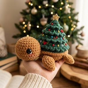 May include: A crocheted turtle plush toy with a tan head and body, featuring a dark green Christmas tree shell decorated with small colorful lights, red berries, and a small yellow star topper. The turtle has a large black eye and pink cheeks.
