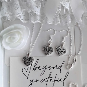 May include: A silver necklace and earrings set with a delicate heart pendant. The jewellery is displayed on a white card with the text "beyond grateful" and "thank you so much".
