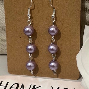May include: A pair of silver dangle earrings with three lavender colored pearl beads on each earring.