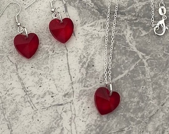 Puede incluir: Un collar de cadena de plata con un colgante de corazón de cristal rojo. También se incluyen pendientes de corazón de cristal rojo a juego.