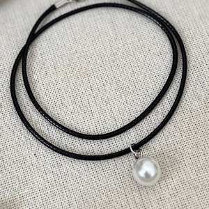 Puede incluir: Un collar choker negro simple con un colgante de perla blanca.