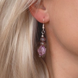 May include: A pair of dangle earrings with a silver hook and multiple purple and clear glass beads. The beads are faceted and have a shimmery finish.