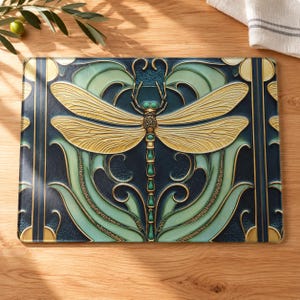 Peut inclure: Une planche à découper rectangulaire en verre ornée d'une libellule centrale aux ailes dorées et au corps vert. Le fond présente des motifs de feuilles tourbillonnantes bleu foncé et vert clair avec des accents dorés symétriques.