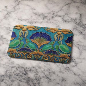 May include: Rectangular teal-colored decorative item with an embossed design featuring turtles, flowers, and ornate gold accents. The turtles are green, and the flowers are blue and gold. The overall design is intricate and detailed.