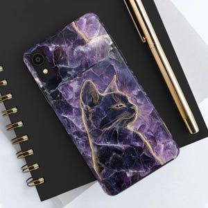 May include: A phone case with a purple, stone-like pattern and a gold outline of a cat. The case is on a black notebook with a gold pen. The phone case has a camera and flash.