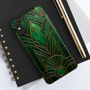 May include: A green and gold phone case with an Art Deco design. The case features a dark green background with gold geometric lines and shapes. The phone case is lying on a black notebook next to a gold pen.