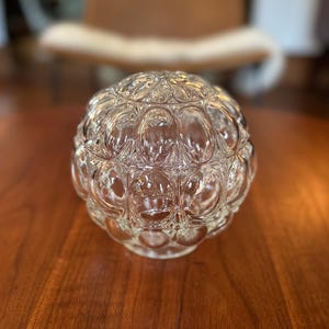 May include: A clear glass light fixture globe featuring a repeating pattern of raised, circular bubble-like indentations across its spherical surface. The glass is transparent and reflects light, creating a textured appearance on the rounded object.