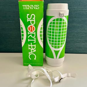 Puede incluir: Un Sport Pac de tenis verde y blanco con una caja y una correa a juego. El recipiente cilíndrico presenta un gráfico de raqueta de tenis. La caja dice "TENNIS SPORT PAC" en letras blancas. La correa es blanca.