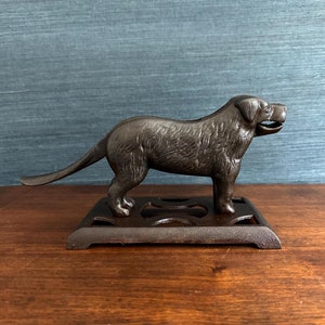 May include: A cast iron dog nutcracker with a detailed design. The dog is standing on a base with a decorative pattern. The nutcracker is painted in a dark brown color.