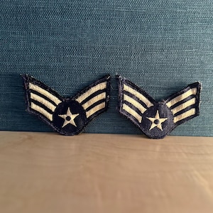 Op de afbeelding: Twee vintage Air Force-patches. Elke patch is donkerblauw met drie witte strepen en een witte ster in het midden. De patches hebben een V-vorm.