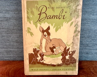 Puede incluir: Libro vintage "Bambi" de Walt Disney. La portada presenta un cervatillo con otras criaturas del bosque. El título "Bambi" está en una elegante escritura. El libro tiene un esquema de color verde y beige con el nombre del autor en la parte inferior.