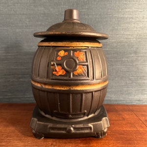 Puede incluir: Jarrón de cerámica negro con forma de estufa de leña con ribete dorado y detalles florales rojos y naranjas.