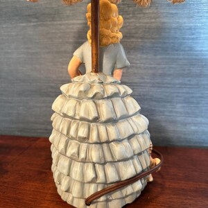 Puede incluir: Una l&aacute;mpara de mesa vintage con una figura de cer&aacute;mica de una mujer con un vestido azul y una falda con volantes. La l&aacute;mpara tiene una pantalla blanca con un borde de flecos.