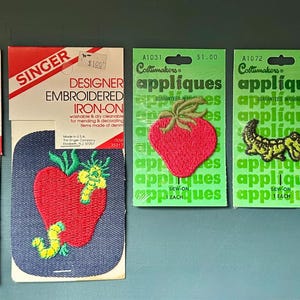 Peut inclure: Cinq écussons brodés vintage à repasser ou à coudre sur leur support en carton d'origine. Deux écussons Singer présentent une coccinelle sur une fleur jaune et une pomme rouge avec des vers verts. Trois écussons Cottmakers montrent une fraise, un crocodile et un papillon.