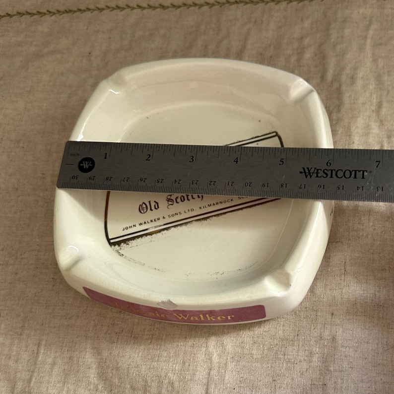 Pode incluir: Cinzeiro de cer&acirc;mica branca com cantos arredondados, com o texto "Old Scotch" e "John Walker & Sons Ltd, Kilmarnock". O cinzeiro mede aproximadamente 15 cm de largura. Uma r&eacute;gua &eacute; colocada sobre o cinzeiro.