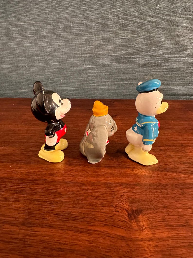 K&ouml;nnte beinhalten: Drei Keramikfiguren von Disney-Charakteren: Micky Maus, Dumbo der Elefant und Donald Duck. Micky ist schwarz mit roten Shorts und gelben Schuhen. Dumbo ist grau mit einem gelben Hut. Donald Duck ist wei&szlig; mit einem blauen Matrosenanzug und Hut.