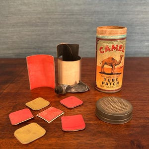 Può includere: Un assortimento di articoli vintage per la riparazione di camere d'aria per biciclette. Include un contenitore Camel Tube Patch con una grafica di cammello, toppe, una raspa di metallo e un tubetto di colla. Gli articoli sono disposti su una superficie di legno.
