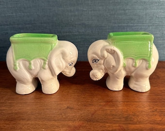 Puede incluir: Dos figuritas de elefante de cerámica blanca con decoraciones verdes en forma de silla de montar. Los elefantes se miran.