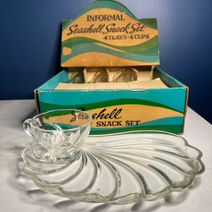 Puede incluir: Un juego de aperitivos vintage en forma de concha en su caja original. El juego incluye cuatro bandejas de vidrio y cuatro tazas, todas con forma de concha. La caja es marrón con acentos azules y verdes y dice "Informal Seashell Snack Set 4 Trays 4 Cups".