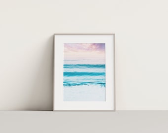 May include: A framed photograph of a seascape with blue and turquoise waves crashing on a white sandy beach. The sky is a soft pink and purple.
