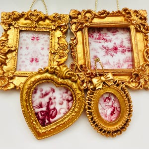 Puede incluir: Conjunto de cuatro marcos de fotos dorados con detalles ornamentados. Los marcos están colgados de un fondo blanco. Los marcos están vacíos, pero tienen un aspecto vintage.