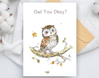Puede incluir: Tarjeta de felicitación con una ilustración en acuarela de un búho marrón y blanco posado en una rama. El texto "Owl You Okay?" está impreso encima del búho. Incluye un sobre marrón.