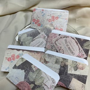 May include: A selection of small paper envelopes with a vintage design. The envelopes are decorated with floral and botanical patterns, and text overlays in various fonts and colours. The colour scheme includes soft pinks, greens, and browns.