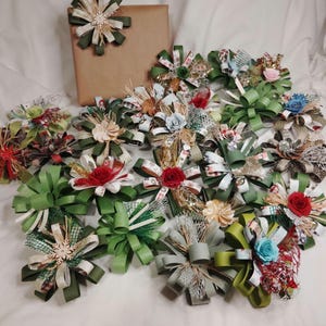 May include: A collection of handmade decorative bows in various colors and designs. The bows feature green, red, white, and gold ribbons, with some adorned with floral accents. A wrapped gift with a matching bow is also present.