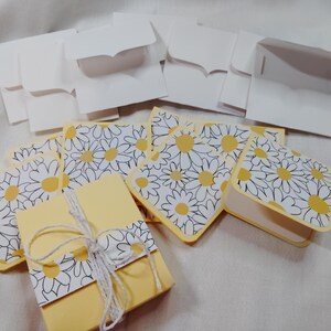 May include: A set of yellow and white gift boxes with a daisy pattern. The boxes are folded flat and ready to be assembled.