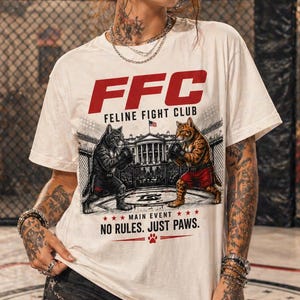 May include: White t-shirt with a graphic of two cats boxing in front of a building, with the text "FFC FELINE FIGHT CLUB" in red. The shirt also features the text "NO RULES. JUST PAWS." and a paw print.