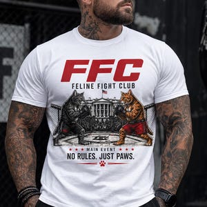 Könnte beinhalten: Weißes T-Shirt mit einem Grafikdesign von zwei boxenden Katzen in einem Ring, mit dem roten Text "FFC FELINE FIGHT CLUB". Darunter steht "MAIN EVENT, NO RULES. JUST PAWS."