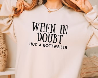 May include: A cream-colored sweatshirt with the text "WHEN IN DOUBT HUG A ROTTWEILER" printed in black.