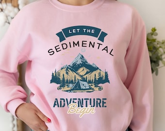 May include: Pink sweatshirt with a graphic design of mountains, a tent, and trees. The text "Let the Sedimental Adventure Begin" is printed on the sweatshirt.