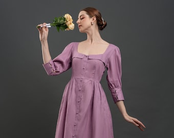 May include: A woman in a lavender maxi dress with a square neckline and button-up front. She is holding a bouquet of yellow roses and smelling them.