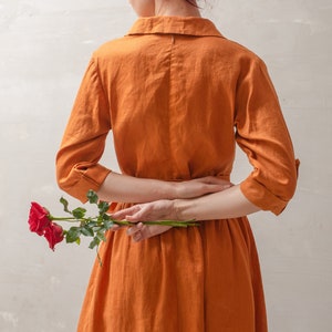 Puede incluir: Una mujer con un vestido de lino color &oacute;xido est&aacute; sosteniendo una sola rosa roja detr&aacute;s de su espalda.
