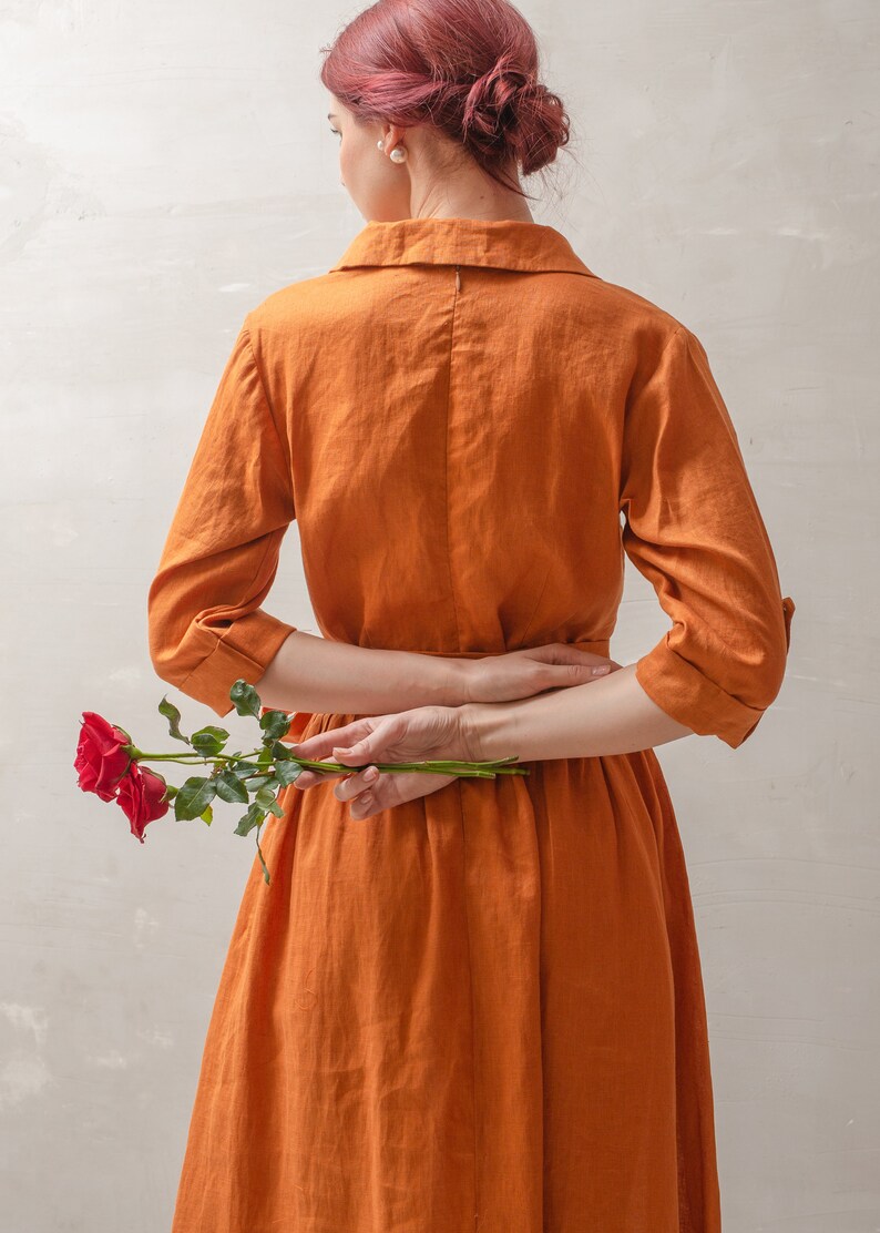 Puede incluir: Una mujer con un vestido de lino color &oacute;xido est&aacute; sosteniendo una sola rosa roja detr&aacute;s de su espalda.