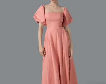May include: A coral-colored midi dress with a square neckline and short, puffed sleeves. The dress features a fitted bodice and a flowing skirt. The model is wearing beige heels. The dress is made of a textured fabric.