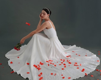 May include: A white wedding dress with a flowing skirt and a simple bodice. The dress is surrounded by red rose petals.