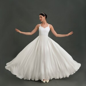 May include: A white sleeveless wedding dress with a full skirt and a sweetheart neckline. The dress is made of a soft, flowing fabric and has a simple, elegant design.