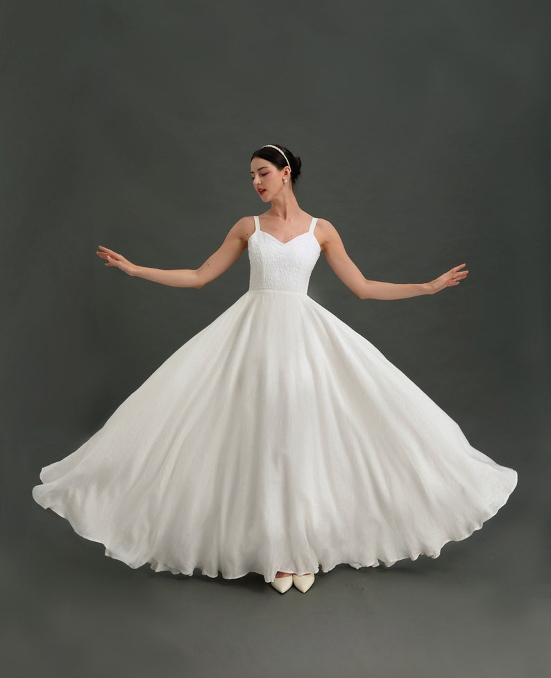 May include: A white sleeveless wedding dress with a full skirt and a sweetheart neckline. The dress is made of a soft, flowing fabric and has a simple, elegant design.