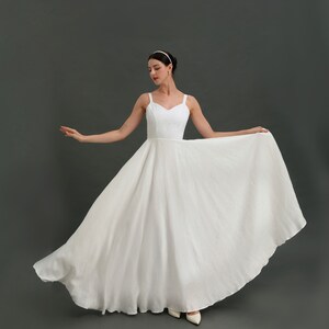 May include: A white sleeveless wedding dress with a sweetheart neckline and a full skirt. The dress is made of a lightweight fabric and has a simple, elegant design.