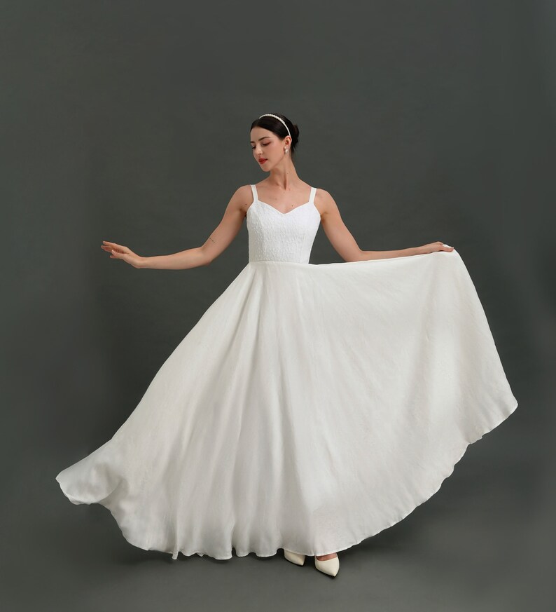 May include: A white sleeveless wedding dress with a sweetheart neckline and a full skirt. The dress is made of a lightweight fabric and has a simple, elegant design.