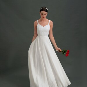 May include: A white sleeveless wedding dress with a sweetheart neckline and a flowing skirt. The bride is holding a bouquet of red roses.