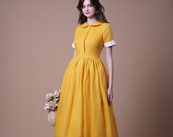 Pode incluir: Vestido midi amarelo mostarda com gola e mangas curtas com punhos brancos. O vestido apresenta cintura ajustada e saia rodada. A modelo segura uma cesta de vime com flores e usa saltos castanhos.