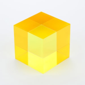 May include: A yellow cube made of acrylic with a gradient of colour from a darker yellow to a lighter yellow.