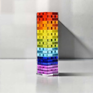 May include: A rectangular, transparent vase with a rainbow gradient design. The colors transition from red at the top to purple at the bottom. The vase is composed of stacked, rectangular blocks.