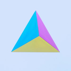 Puede incluir: Un triángulo tridimensional hecho de papel. El triángulo está dividido en tres secciones, cada una de un color diferente: azul, amarillo y rosa.