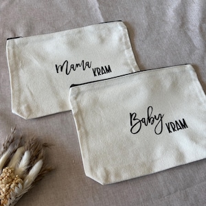 Könnte beinhalten: Zwei cremefarbene Canvas-Reißverschlusstaschen. Eine Tasche hat die Worte "Mama Kram" in schwarzer Schrift, die andere "Baby Kram". Beide Taschen haben schwarze Reißverschlüsse.