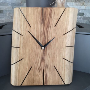 May include: A wooden clock with black hands and a unique design. The clock face is made of natural wood with a rustic finish. The clock is a square shape with rounded corners.